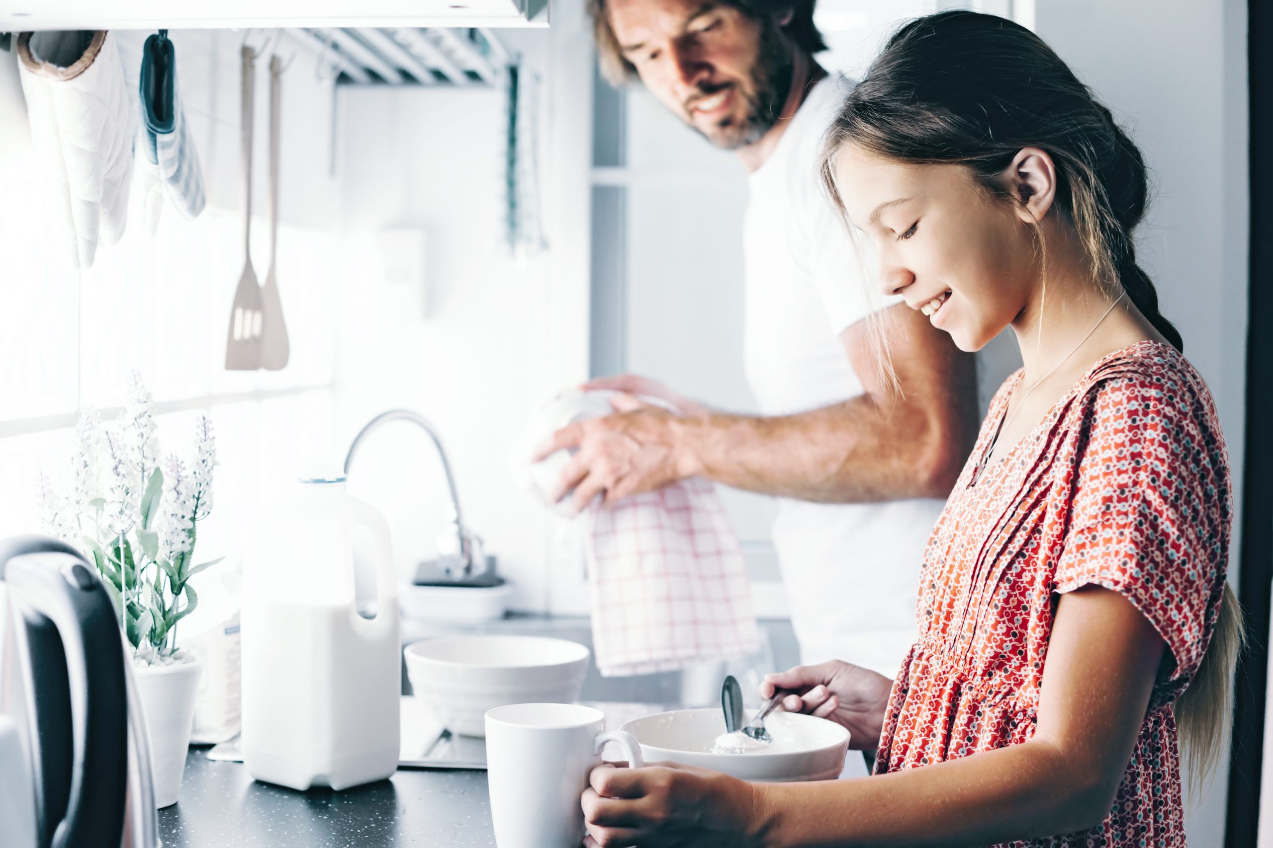 Dad with his 10 years old kid girl cooking in the kitchen, casual lifestyle photo series. Child making breakfast with parent together. Cozy homely scene.